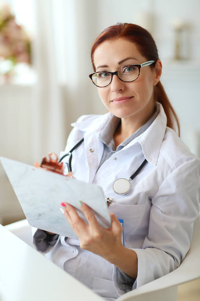 Νοσοκομείο και ιατρική έννοια. Γυναίκα γιατρός με κοκκινομάλλα που εργάζεται στην κλινική - Φωτογραφία, εικόνα
