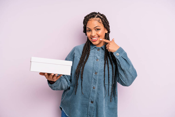 black afro woman smiling confidently pointing to own broad smile. packages box concept - Photo, image