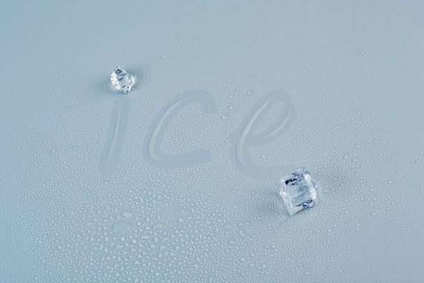 Inscription ice on a wet gray background with two ice cubes - Foto, afbeelding