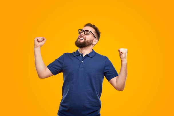 Satisfied young guy with clenched fists celebrating victory in yellow studio - Фото, зображення