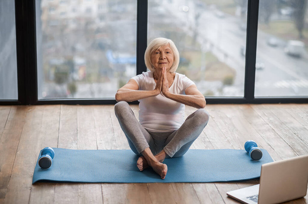 Gray-haired senior woman sitting on the floor and meditating - Foto, immagini