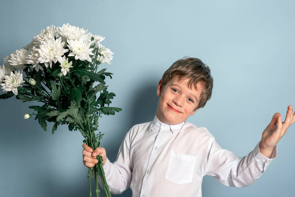 A cute Caucasian boy in a white shirt holds a bouquet of white flowers in his hand and smiles. - Valokuva, kuva