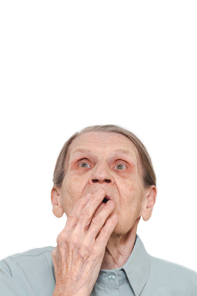 Lifestyle portrait of an elderly woman with a hand covering her mouth on a white background. Surprised old lady pensioner with a frightened expression on her face. Concept of emotional shock. - Photo, image
