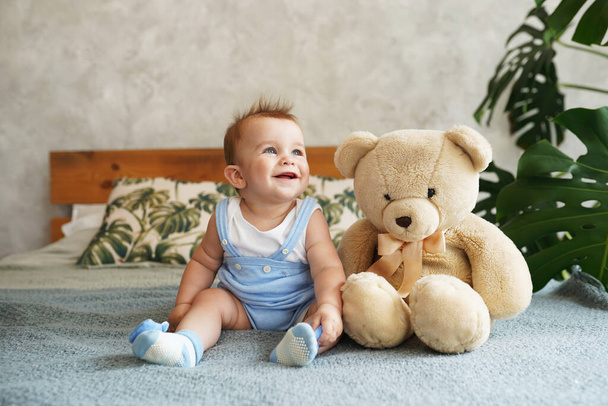 Χαριτωμένο μωρό παίζει με αρκουδάκι στο κρεβάτι στο σπίτι στο φως δωμάτιο - Φωτογραφία, εικόνα
