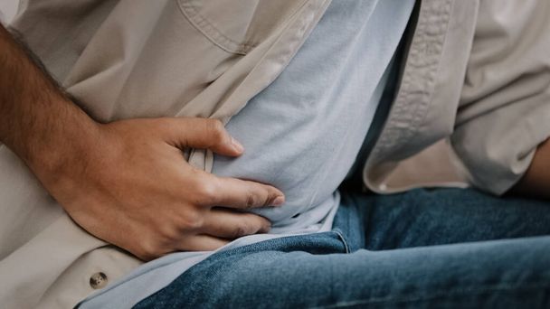 Close-up of male hands holding belly by side unrecognizable man feels bad digestive problems abdominal pain illness suffers from liver damage bending body in ache feeling unwell poisoning concept - Photo, image