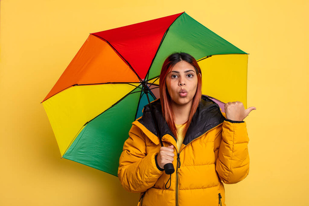 hispanic woman looking astonished in disbelief. rain and umbrella concept - Foto, Imagem
