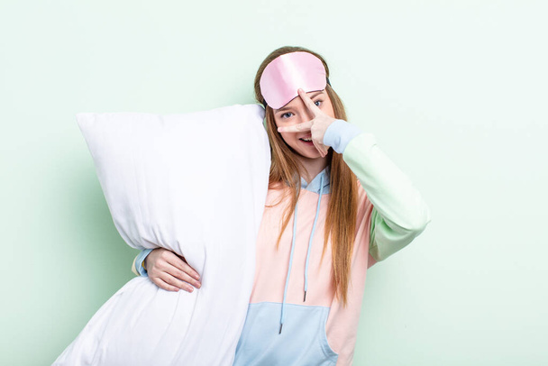 redhair woman looking shocked, scared or terrified, covering face with hand. pajamas and pillow concept - Photo, image