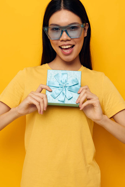 Charming young Asian woman yellow t-shirts birthday gift box isolated background unaltered - 写真・画像