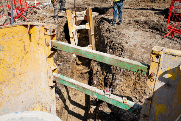 Ground workers installing trench support safety shoring system during deep drainage works on new residential housing development construction site - Foto, immagini