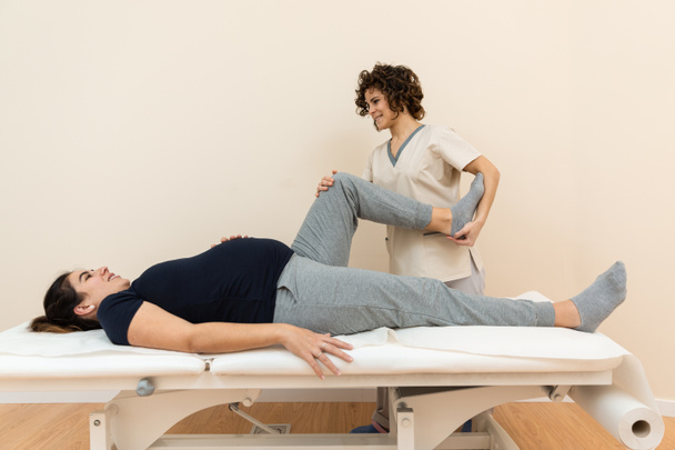 Fizyoterapist bir sağlık merkezinde bacaklarına masaj yaparken, hamile bir kadın masaj masasında yatıyor. - Fotoğraf, Görsel