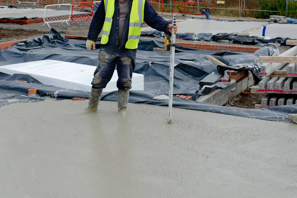 Concreter checking level of the concrete using laser level and staff as he pour ground floor slab of the new residential house - Photo, Image