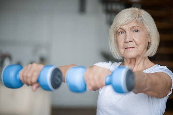 Active senior woman with dumbbells in hands doing her workout - Foto, imagen