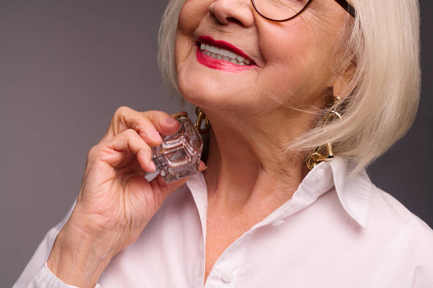 Талія старшої жінки з парфумами в руках
 - Фото, зображення