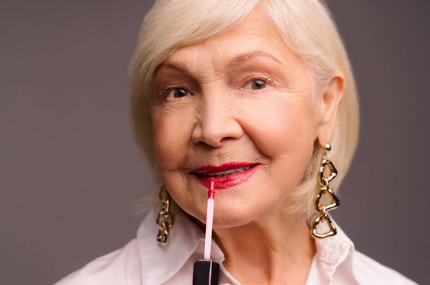 Blonde stylish senior woman putting lip gloss on her lips - Fotoğraf, Görsel