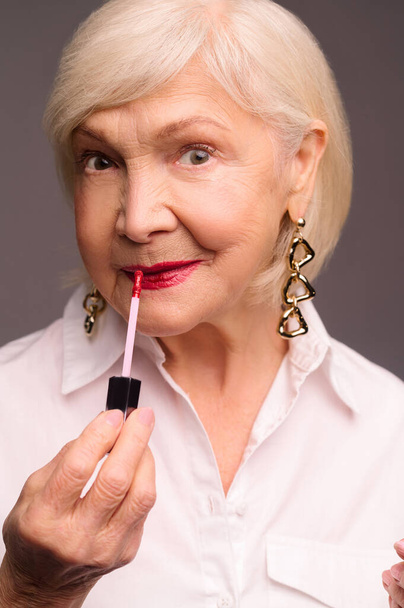 Блондинка стильна старша жінка кладе блиск для губ на губи
 - Фото, зображення