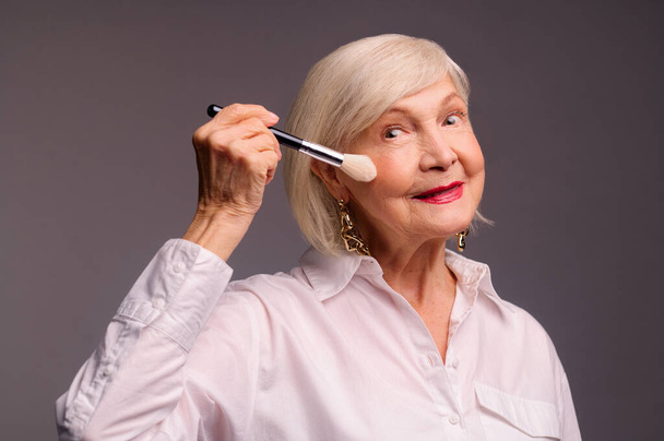 Stylish elegant senior woman holding a face brush - Foto, Imagen