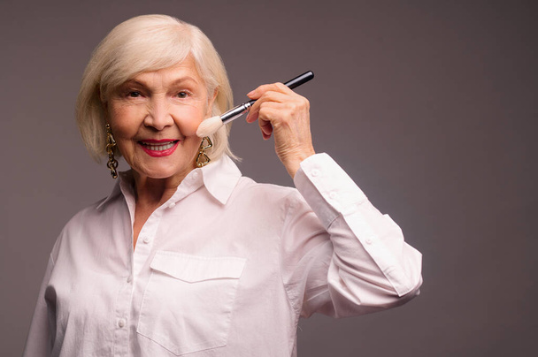 Stylish elegant senior woman holding a face brush - Foto, Imagen