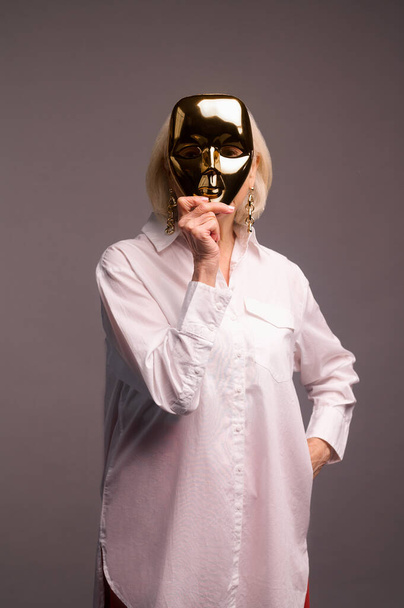 A woman in white shirt holding a masquerade mask - Фото, изображение
