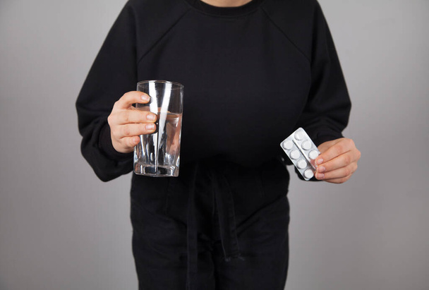 Hasi fájdalomtól szenvedő fiatal nő. Tabletták és pohár víz. Szürke háttér. - Fotó, kép