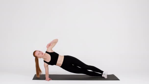 Athlétique jeune femme faisant side Planche Rotations exercice tout en s'entraînant en studio - Séquence, vidéo