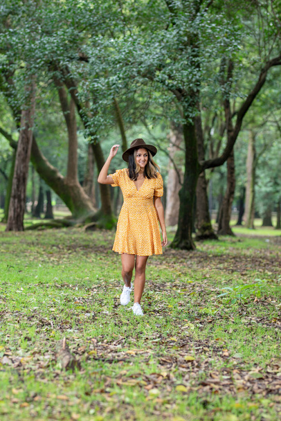 Latin woman with dress and hat walking through a park with trees - Foto, Imagen