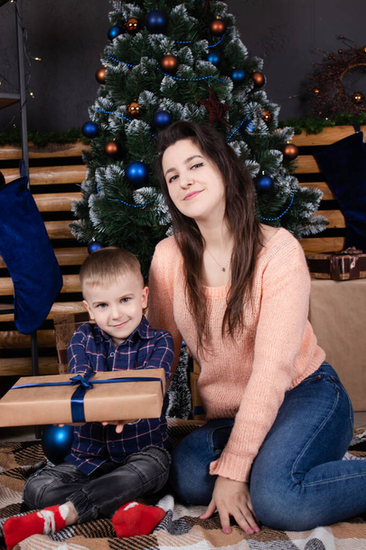 クリスマスツリーと装飾の近くの女性と小さな幼児の男の子。息子と母はクリスマス・イヴに。新年だ。シングルマザー。不完全な家族 - 写真・画像
