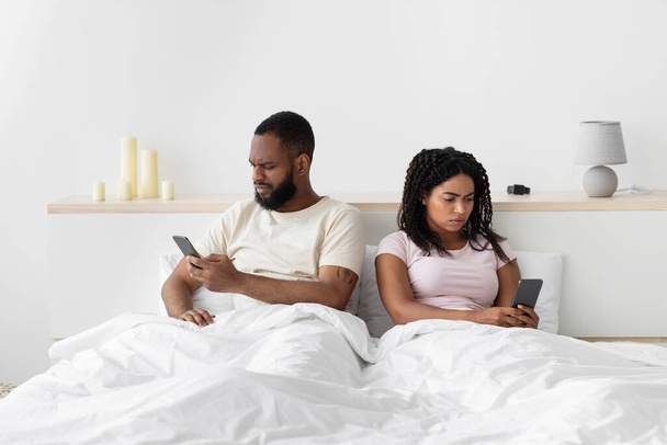 Ображений сумний молодий афроамериканець ігнорує леді і друкує смартфони на зручному ліжку. - Фото, зображення