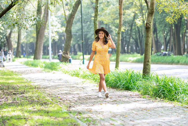 Жінка в жовтій сукні ходить уздовж тротуару в парку
 - Фото, зображення