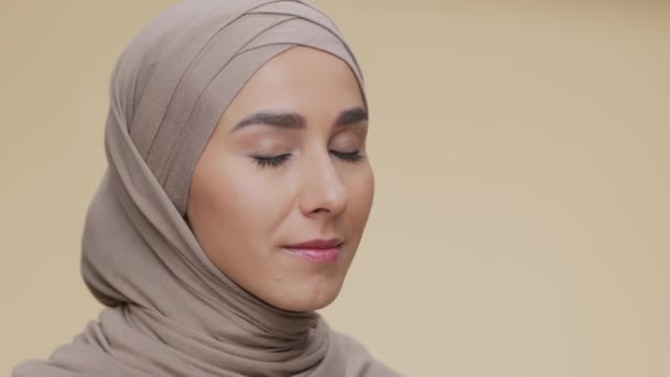 Bellezza musulmana. Bella signora felice mediorientale in velo sorridente alla macchina fotografica su sfondo beige, spazio vuoto - Filmati, video
