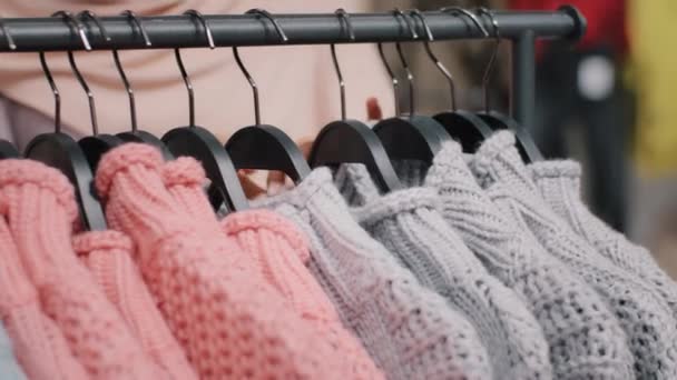 Clothing store close-up of clothes hanger with bright colored sweaters female hands of unrecognizable girl chooses garments in shopping mall fashionable design quality material discount purchase sale - Filmmaterial, Video