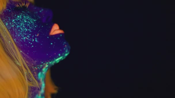 Mujer joven con brillante maquillaje de neón brillante con peluca naranja bailando sobre fondo de estudio negro, espacio vacío - Metraje, vídeo