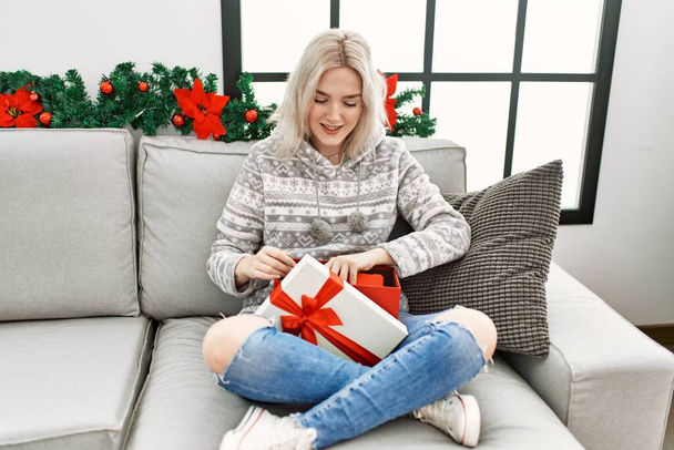 Young caucasian girl smiling happy opening christmas gift at home. - Zdjęcie, obraz