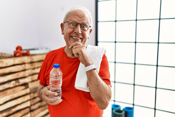 Senior man wearing sportswear and towel at the gym with hand on chin thinking about question, pensive expression. smiling and thoughtful face. doubt concept.  - Foto, immagini