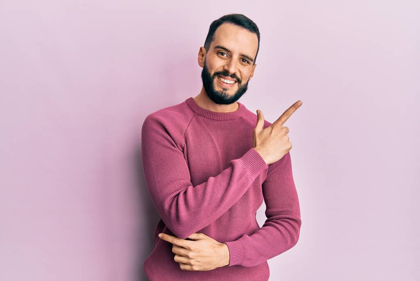 Молодий чоловік з бородою в повсякденному зимовому светрі посміхається весело вказуючи рукою і пальцем в сторону
  - Фото, зображення