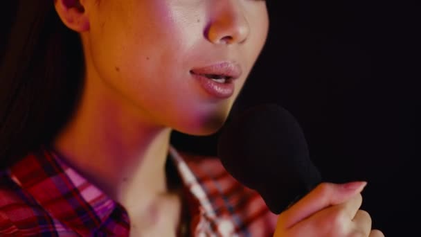 Κοντινό πλάνο Πορτρέτο της νεαρής Ασιάτισσας που τραγουδάει σε μικρόφωνο σε σκούρο φόντο - Πλάνα, βίντεο