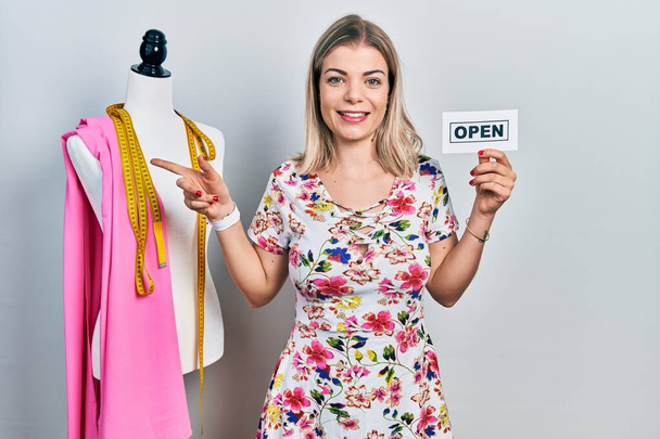 Beautiful caucasian woman dressmaker designer holding open sign smiling happy pointing with hand and finger to the side  - Photo, Image