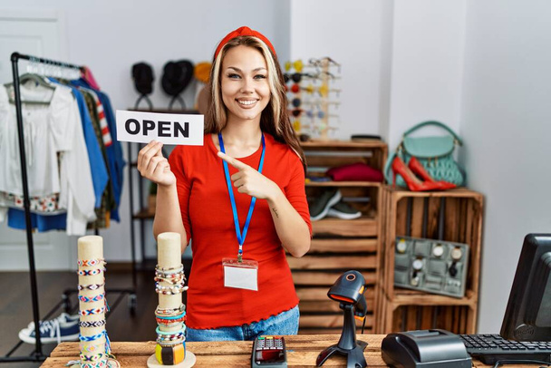 Young caucasian woman holding banner with open text at retail shop smiling happy pointing with hand and finger  - Photo, Image