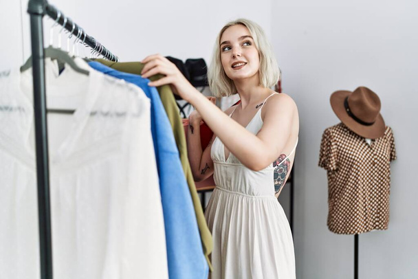 Молода біла жінка посміхається впевнено купує в магазині одягу
 - Фото, зображення