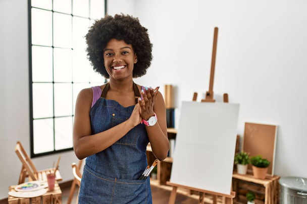 Jovem afro-americana com cabelo afro no estúdio de arte batendo palmas e aplaudindo felizes e alegres, sorrindo mãos orgulhosas juntas  - Foto, Imagem