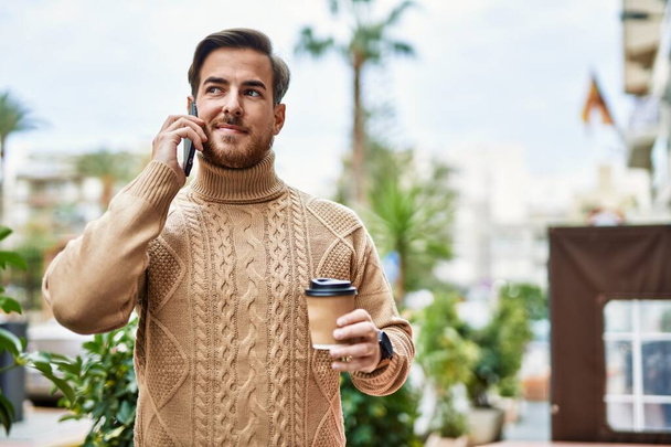 Joven hombre caucásico hablando en el teléfono inteligente beber café en la ciudad. - Foto, imagen