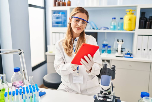 Junge blonde Frau in Wissenschaftleruniform mit Laptop im Labor - Foto, Bild