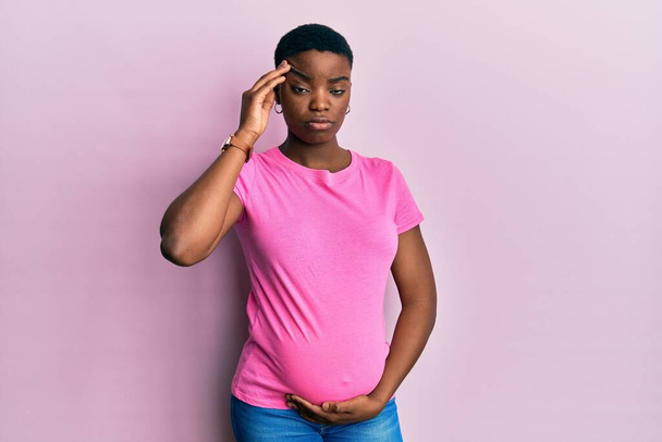 Young african american woman expecting a baby, touching pregnant belly worried and stressed about a problem with hand on forehead, nervous and anxious for crisis  - Fotoğraf, Görsel