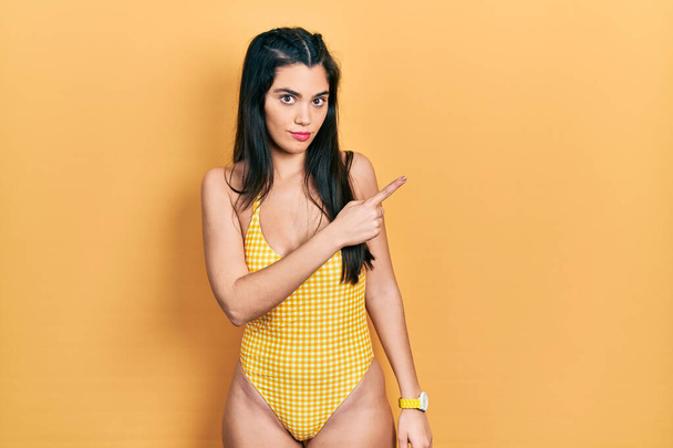 Young hispanic girl wearing swimsuit pointing with hand finger to the side showing advertisement, serious and calm face  - Foto, Bild