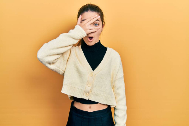 Young brunette girl wearing casual yellow jacket peeking in shock covering face and eyes with hand, looking through fingers afraid  - Photo, Image