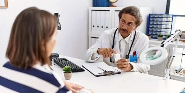 Мужчина и женщина среднего возраста в форме врача имеют медицинскую консультацию проведение таблетки в клинике - Фото, изображение