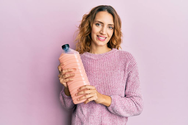Young caucasian woman holding laundry softener bottle looking positive and happy standing and smiling with a confident smile showing teeth  - Photo, Image