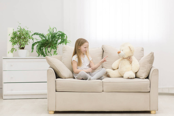 Photo of little girl in white clothes talking to teddy bear. - Фото, изображение