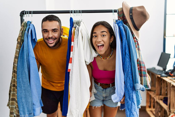 Молодая латинская пара улыбается счастливо появляясь через одежду в магазине моды. - Фото, изображение