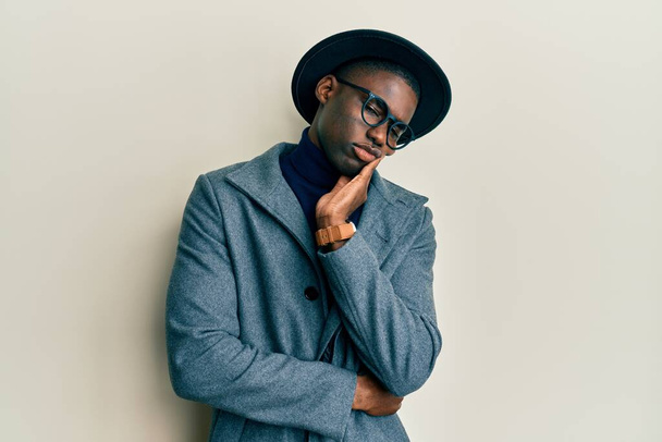 Νεαρός Αφροαμερικάνος που φοράει κομψό στυλ σκέψης φαίνεται κουρασμένος και βαριέται με προβλήματα κατάθλιψης με σταυρωμένα χέρια.  - Φωτογραφία, εικόνα