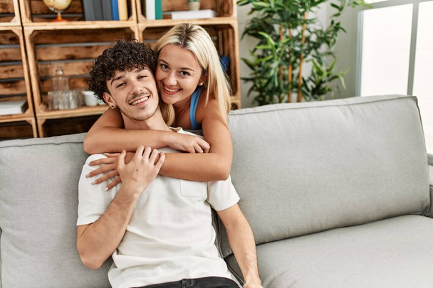 Young couple sitting on the sofa hugging at home. - Фото, зображення